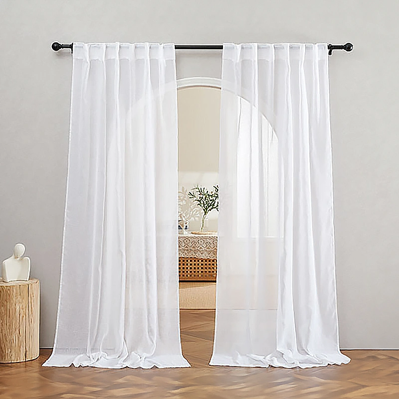 White semi-sheer linen curtains hanging from a black curtain rod in a well-lit room, partially open to reveal a cozy interior.