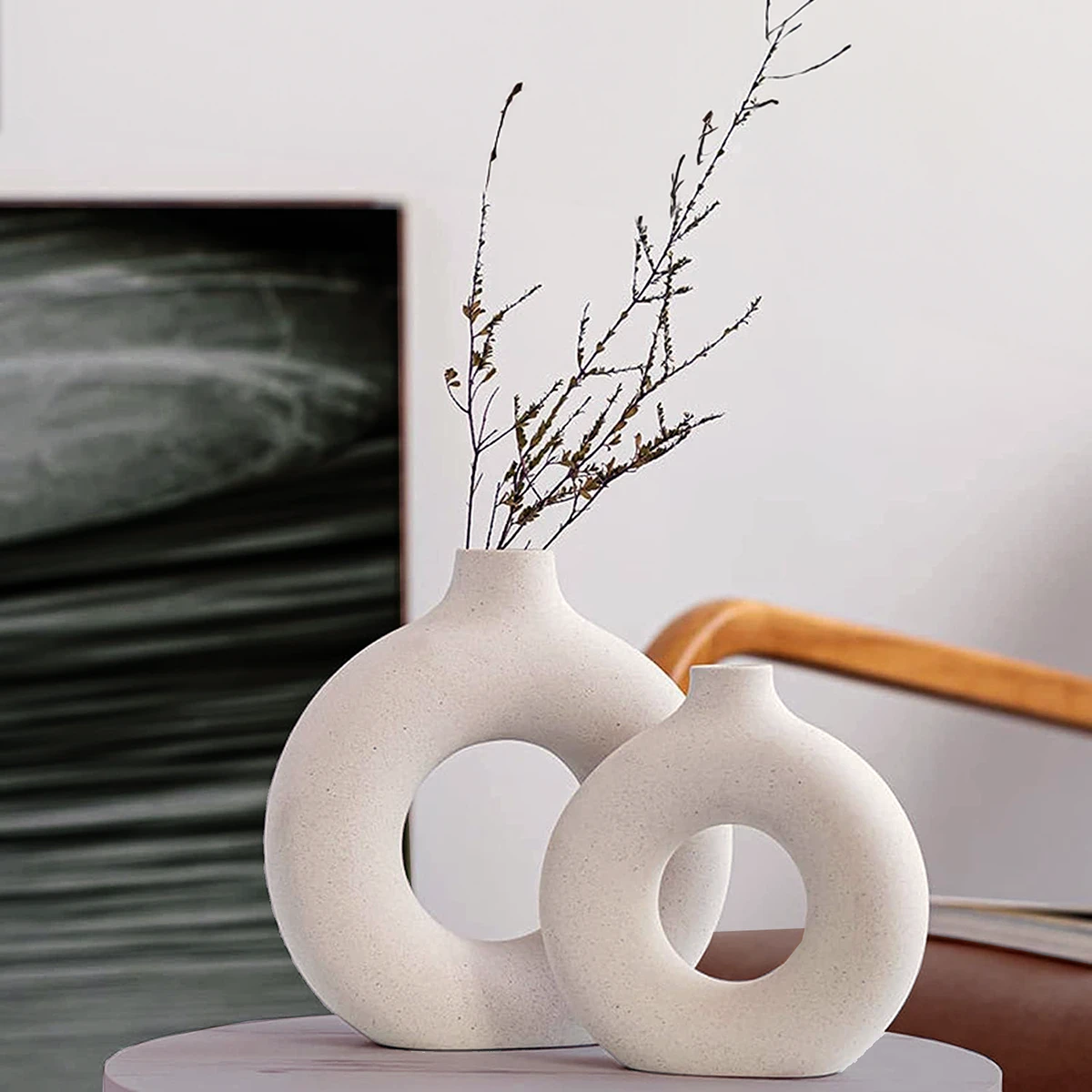 Modern white donut-shaped ceramic vase with a sprig of dried branches, exemplifying contemporary home decor.