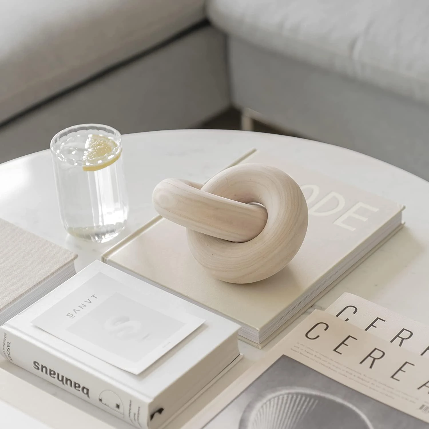 A hand-carved 2-link wood knot decor displayed on a coffee table alongside a stack of books and a glass of water with lemon.