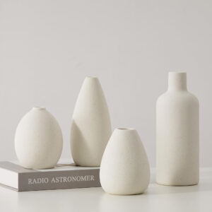 A set of four white ceramic vases placed on a book titled "Radio Astronomer," creating a clean, contemporary aesthetic.