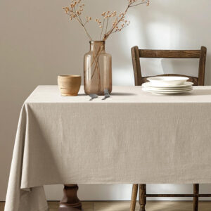 A rustic wooden dining table with a beige linen tablecloth, simple dinnerware, and ceramic accents.